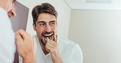 Bearded man brushing his teeth in bathroom mirror