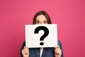 Woman holding up a sign with a question mark so that it covers her mouth